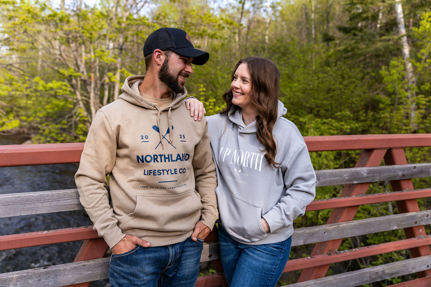 Stylish couple wearing the NLC Twin Paddles Hoodie - Men’s on a bridge surrounded by greenery. Perfect for outdoor adventures.