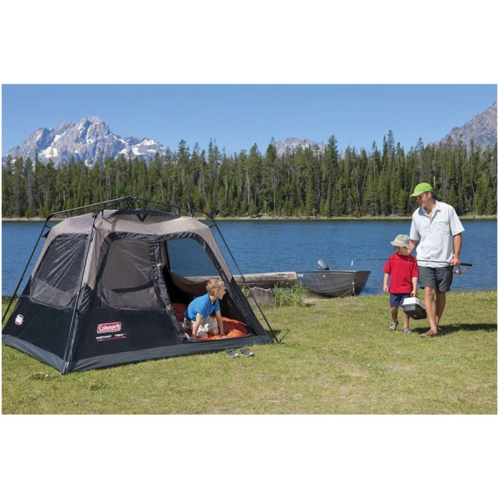 Camping scene with a tent by a lake, mountains, and people around.
