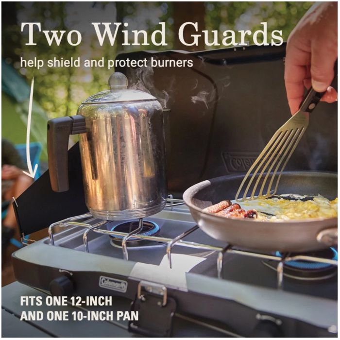 Camp stove with two wind guards, a pot, and a pan being used outdoors.