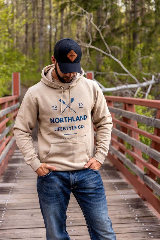 Stylish NLC Twin Paddles Hoodie - Men’s from Northland Lifestyle Co., perfect for outdoor adventures on a wooden bridge.