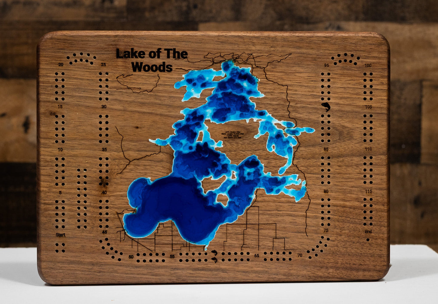 Wooden cribbage board with a map of Lake of The Woods in blue on a wooden background.