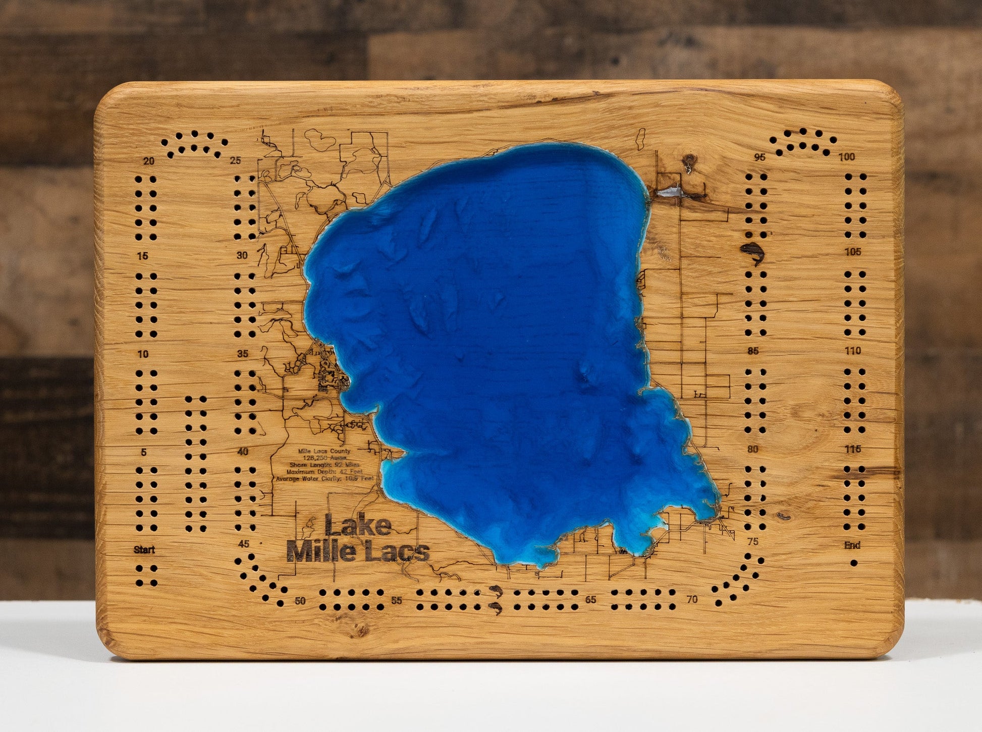 Wooden cribbage board with a blue lake inset, labeled 'Lake Mille Lacs', on a wooden surface.