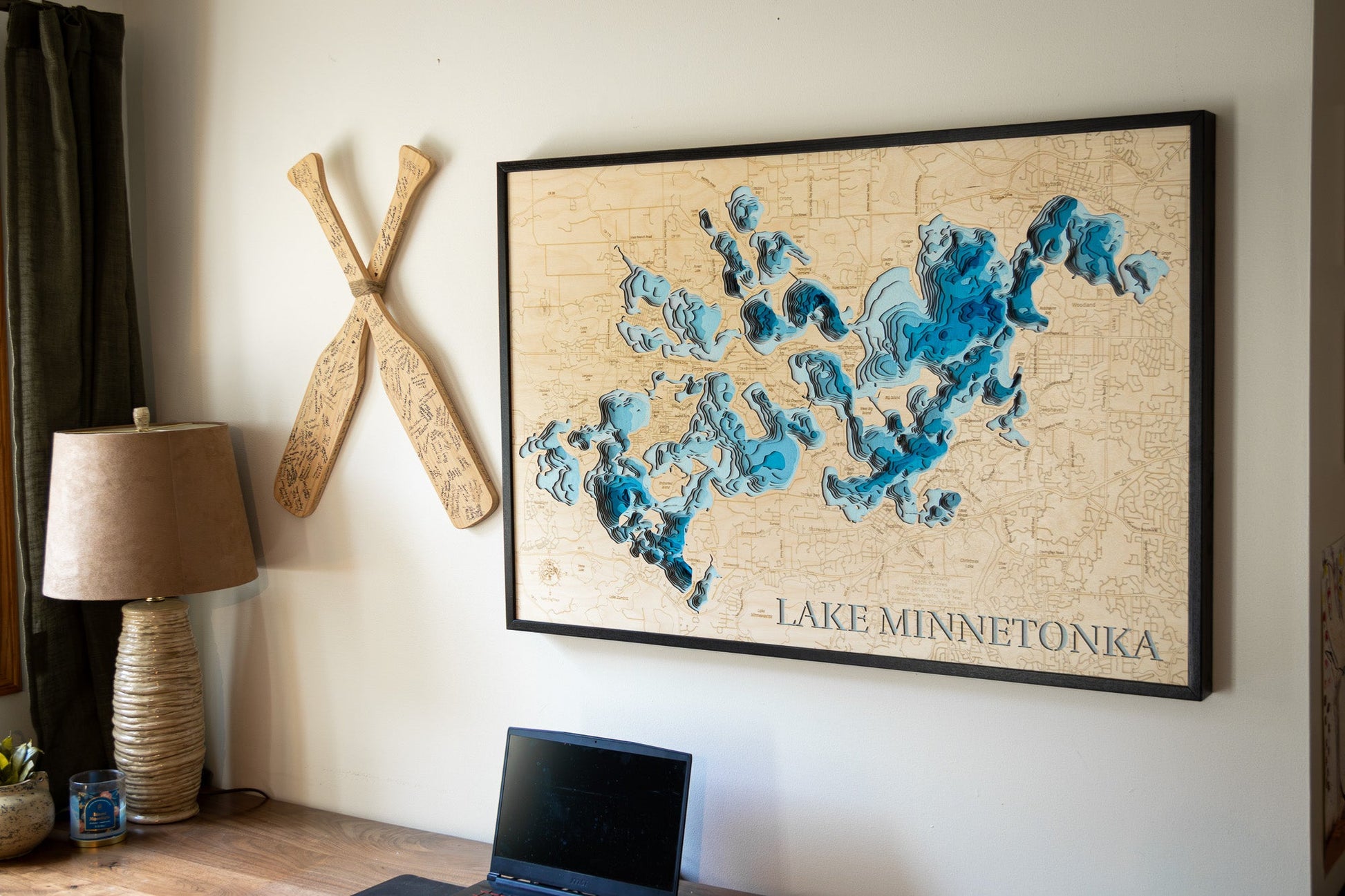 Framed map of Lake Minnetonka on a wall with decorative paddles and a lamp.