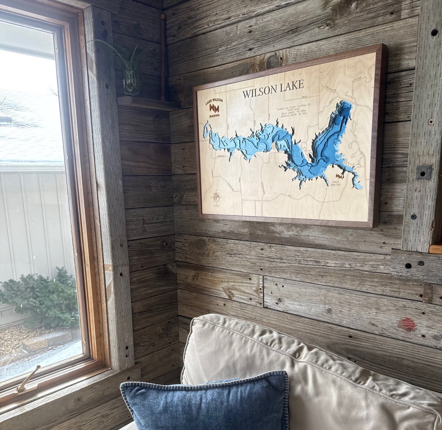 Framed map of Wilson Lake on a wooden wall with a window and cushioned bench in the foreground.